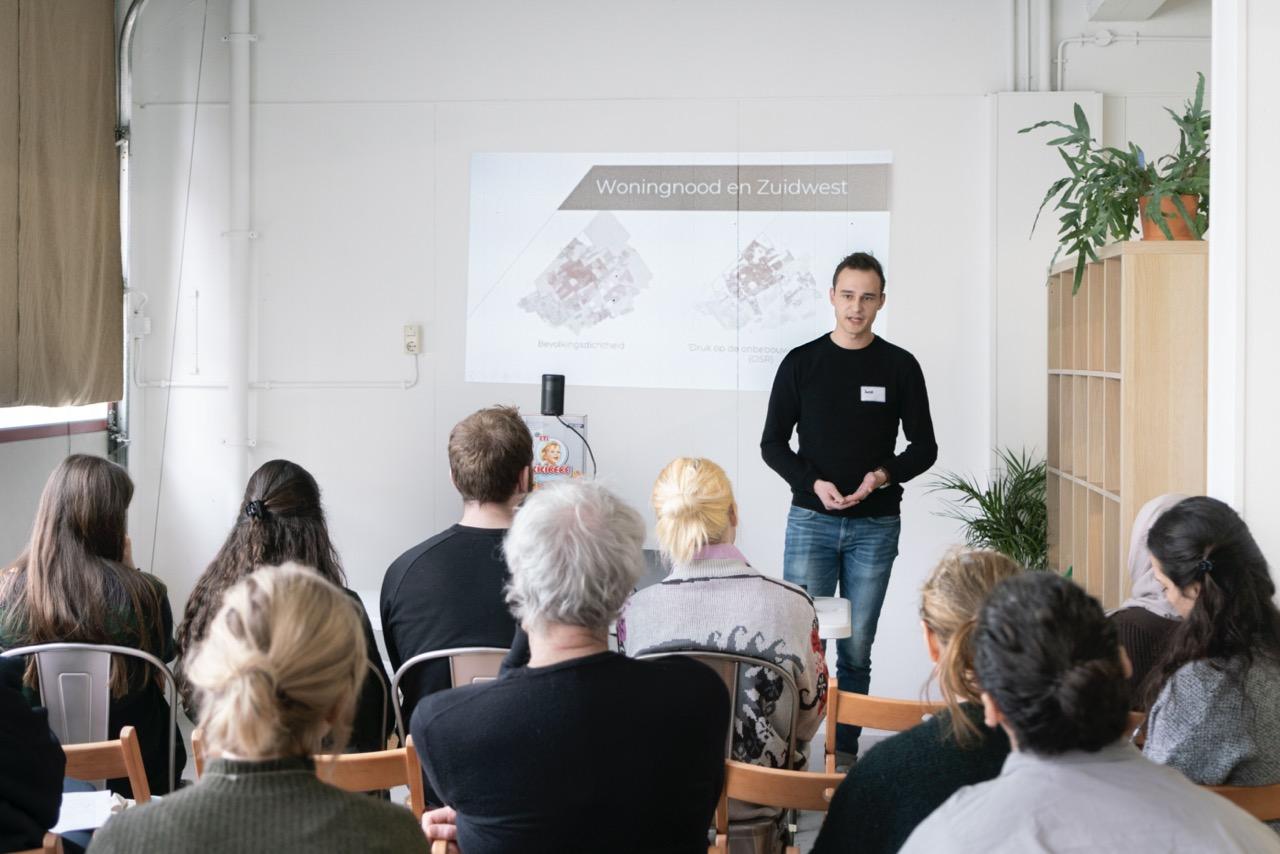 Joost presenting to the audience, wears a black shirt. The audience is in the fore of the image.